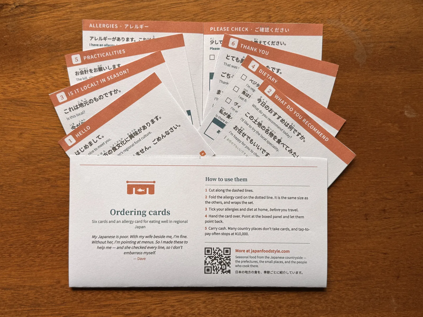 The printed ordering cards fanned on a wooden table: Hello, What do you recommend, Is it local, Dietary, Practicalities, Thank you, and the folding allergy card