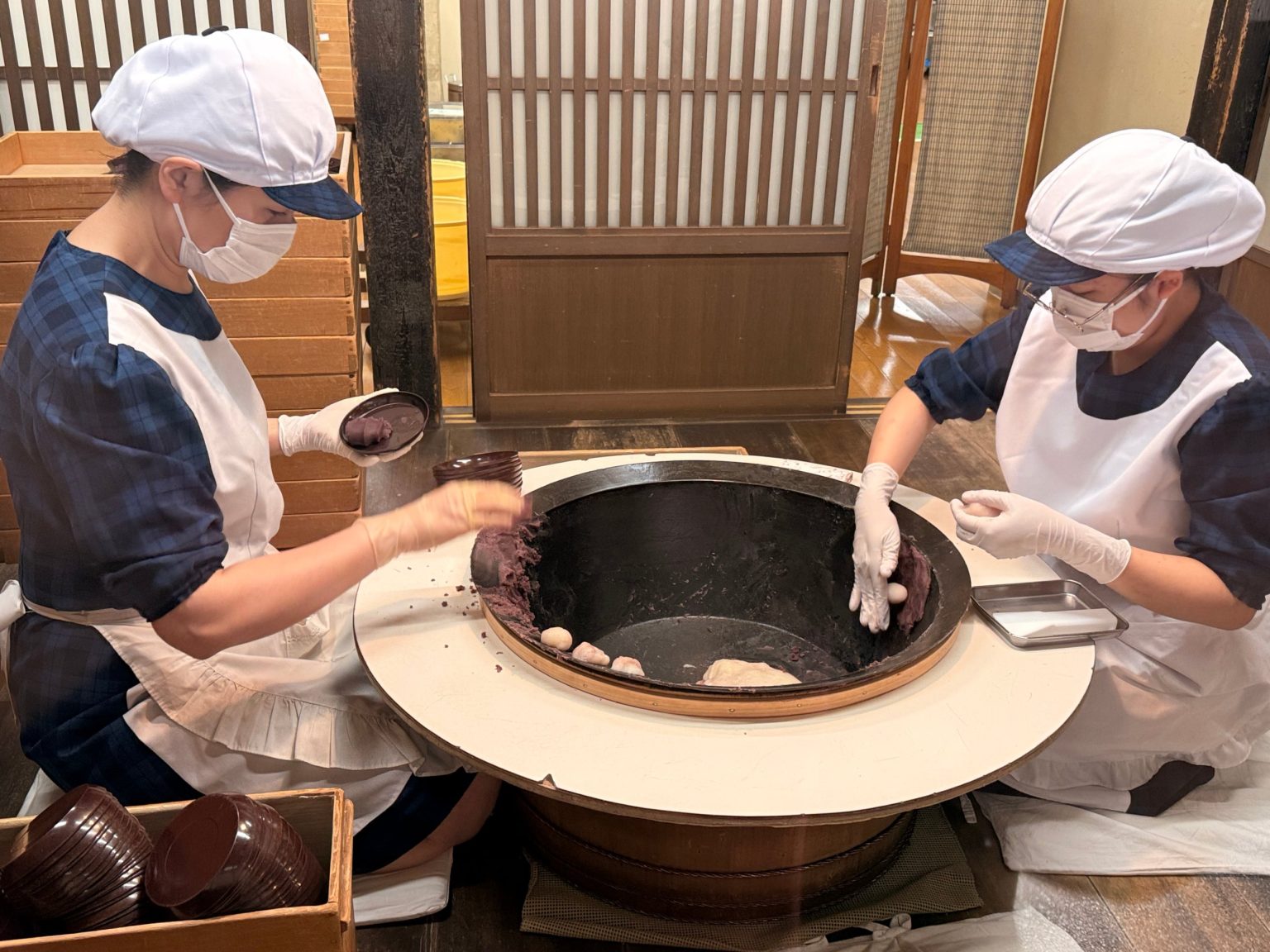 Two staff kneeling at a large iron pot, pressing red bean paste onto mochi by hand at Akafuku