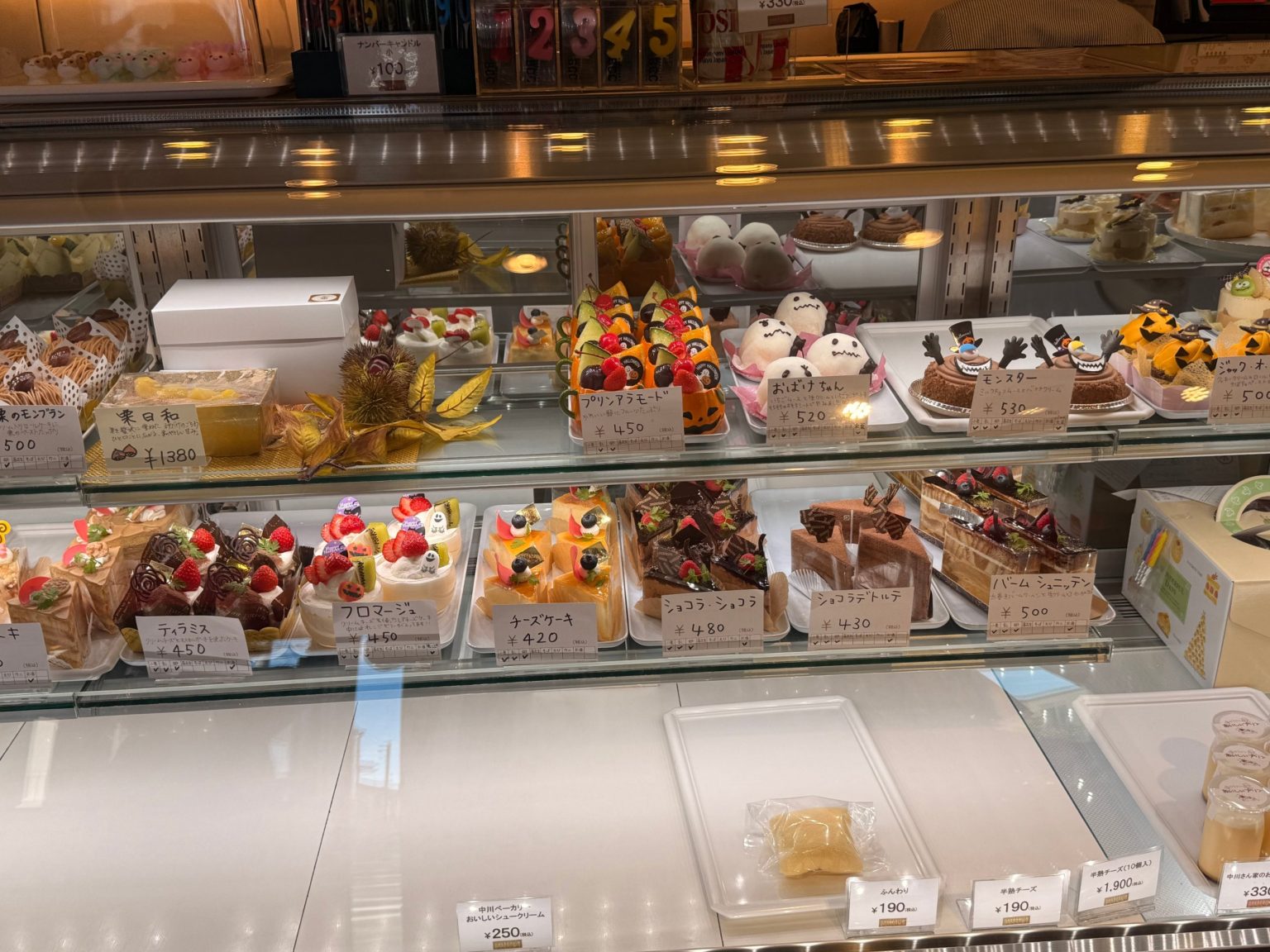 Halloween and classic cakes in the case at Nakagawa Bakery, each with a handwritten price card