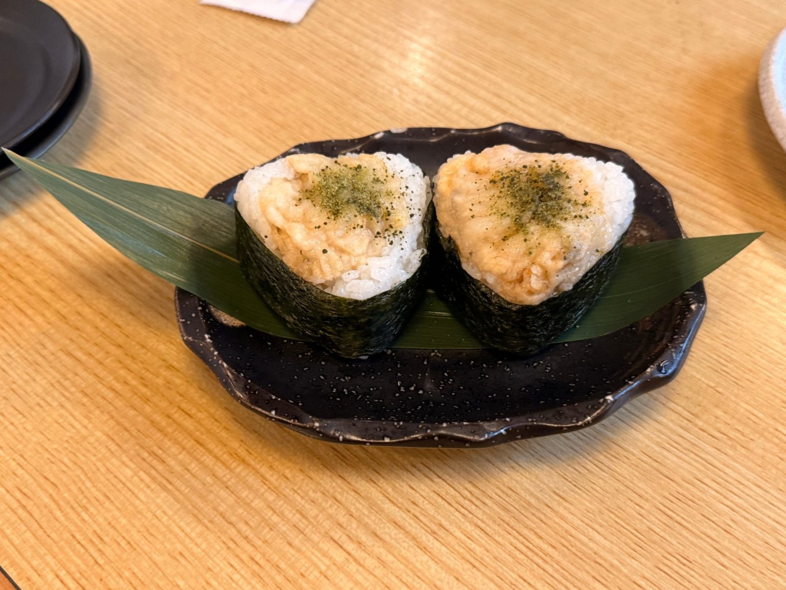 Two hamaguri tenmusu rice balls topped with tempura clam on a bamboo leaf at Kawaichi, Kuwana