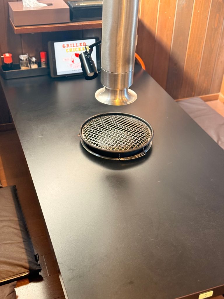 Round grill set into a black table with a steel smoke extractor above it at Shinya, Matsusaka