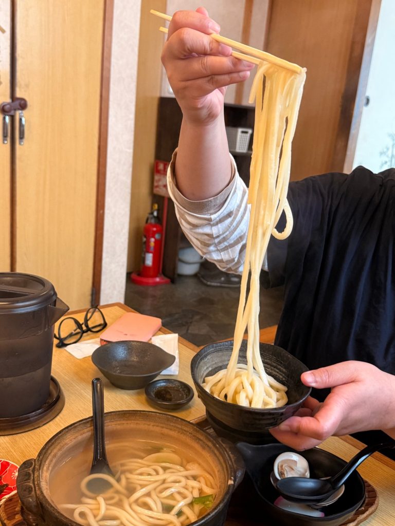 Extra-long udon noodles lifted with chopsticks from a hamaguri hotpot at Kawaichi, Kuwana